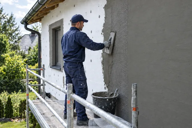 Fachowiec na rusztowaniu zatapia siatkę w kleju na styropianie